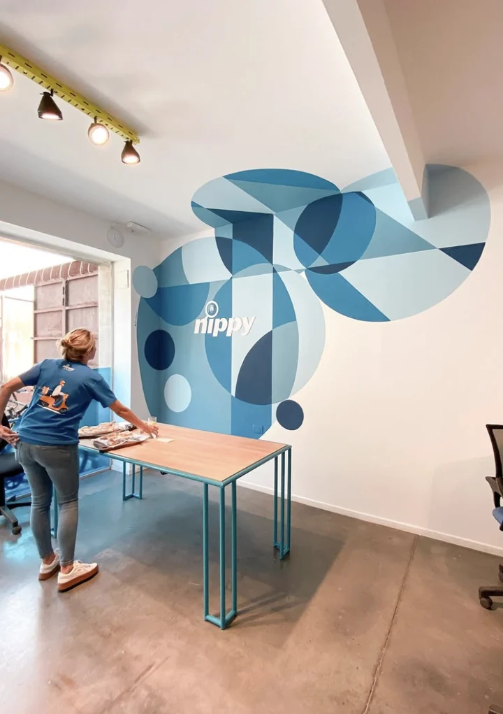 Sala de reuniones con el mural geométrico azul continuando detrás de una mesa de trabajo